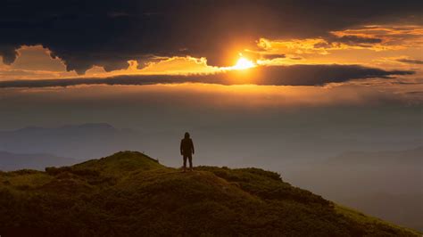 The Man Standing On A Mountain Top Against The Bright Sunrise Time