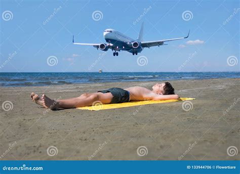 Teen Boy Lies On Yellow Towel And Sunbathes On The Beach Under The