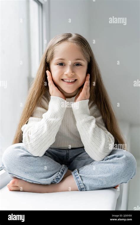 Cheerful Barefoot Girl Looking At Camera While Sitting With Crossed Legs On Windowsill Stock