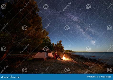 Woman Having A Rest At Night Camping Near Tourist Tent Campfire On Sea