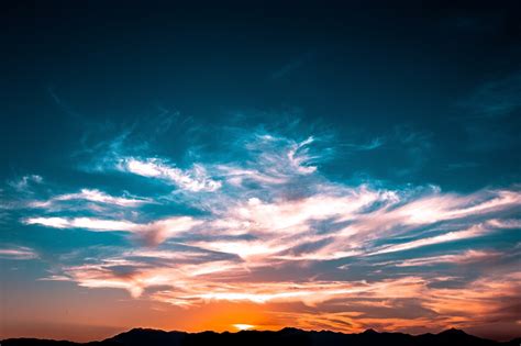 Wispy Clouds Against The Illuminated Orange And Blue Sky With The Sun