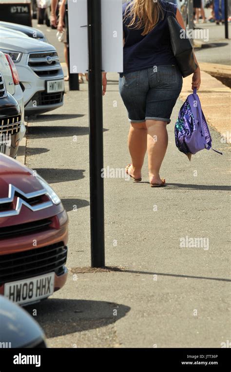 A Fat Or Obese Woman Walking Along A Seafront Pathway Carrying A Bag Of