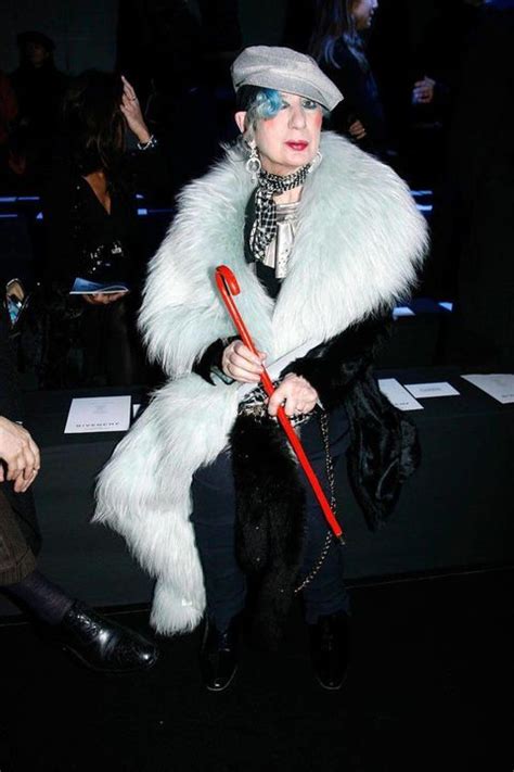 A Woman Sitting In Front Of A Crowd Wearing A Fur Coat And Holding A