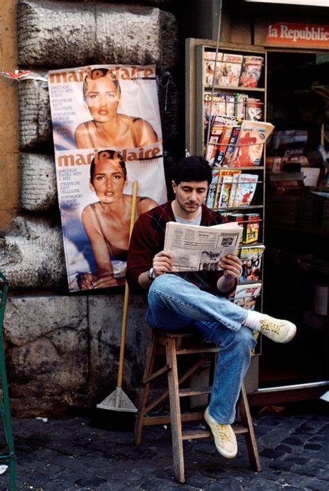 A Man Sitting On A Stool Reading A Newspaper In Front Of A Magazine