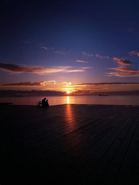 Silhouette Of 2 People Sitting On Wooden Dock During Sunset Photo