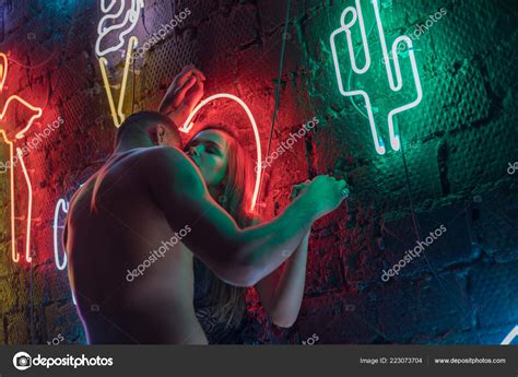 Apasionada pareja desnuda besándose en el fondo de las lámparas de neón