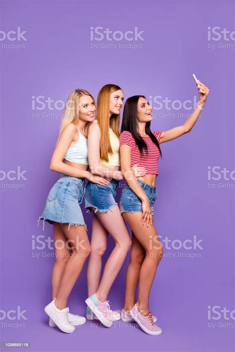 청바지에 매력적인 명랑 소녀 들의 전신 초상화 얇은 다리는 밝은 보라색 배경에 고립 된 스마트 휴대 전화를 사용 하 여 전면 카메라에 selfie를 촬영 하는 데 치마