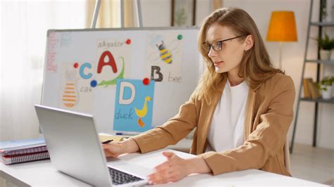 Medium Shot Of Young Female Primary Teacher In Glasses Sitting At Her