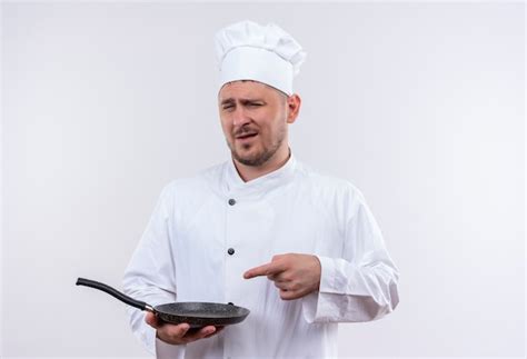 Free Photo Confident Young Handsome Cook In Chef Uniform Holding And Pointing At Frying Pan