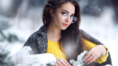 beautiful girl model is standing in blur snow field background wearing specs and yellow woolen