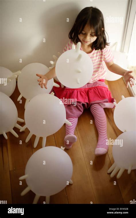 Girl Aged Four Plays With Inflated White Latex Rubber Gloves Sitting On Wooden Hallway Floor