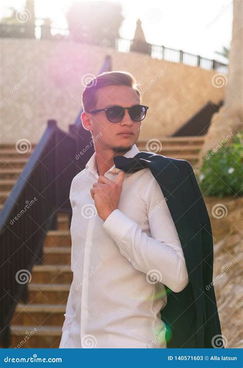 Young Guy In A White Shirt And Sunglasses Stands And Smiles Near The