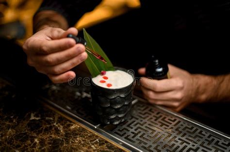 Male Bartender Drop An Essence To A A Glass With Cocktail Decorated With A Green Tropical Leaf