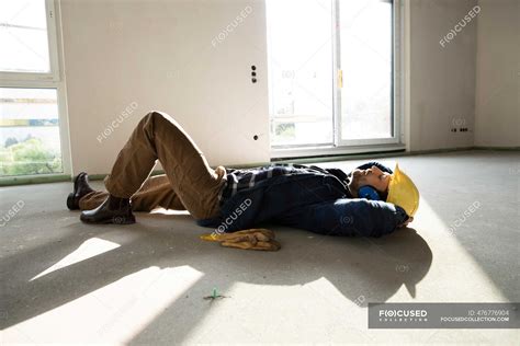 Construction Worker With Hands Behind Head Sleeping On Floor In House