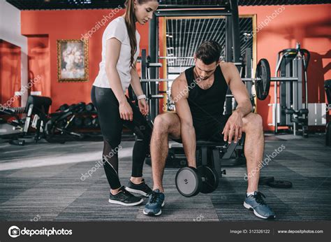 Attractive Trainer Supervising Handsome Sportsman Working Out Dumbbell