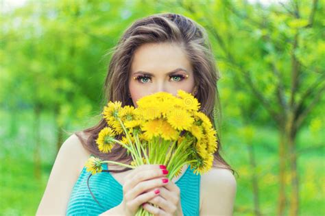 beautiful girl in a sunny summer day walking in the garden and keeps yellow dandelions in the