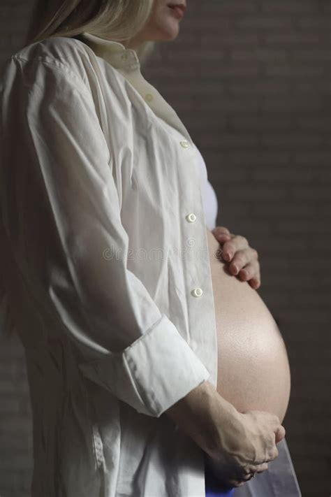 Close Up Of A Pregnant Woman In A White Shirt Gently Stroking Her Stomach With Her Hands In The