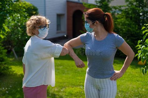 Women In Medical Masks Greet Their Elbows Outside An Elderly Woman And