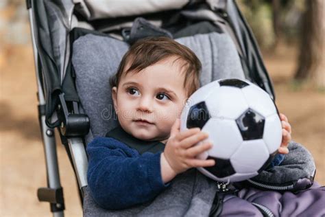 Little Kid Holding A Soccer Ball While Sitting In The Stroller Pram