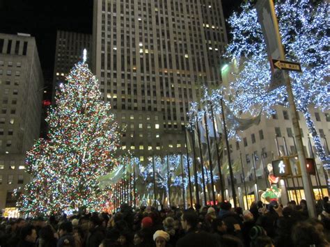 A Large Group Of People Standing Around A Christmas Tree In The Middle