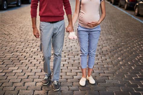 Young Expectant Parents Holding Hands While Posing With Baby Booties