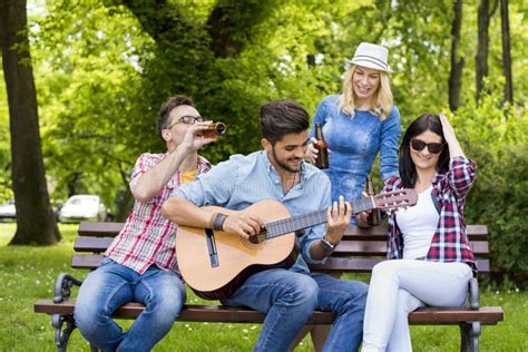 Group Of Young Friends Playing Guitar And Drinking Beers On A Park