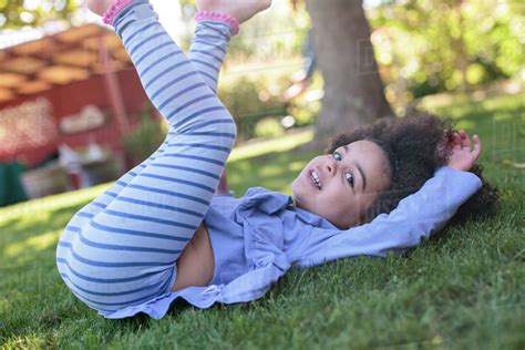 Portrait Of Young Girl Lying On Grass Legs Raised Stock Photo