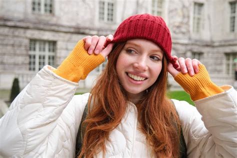 Portrait Of Smiling Redhead Woman Puts On Red Hat And Smiles Wearing Warm Clothes While