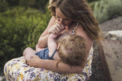 Mother Breastfeeding Daughter While Sitting Against Plants In Forest