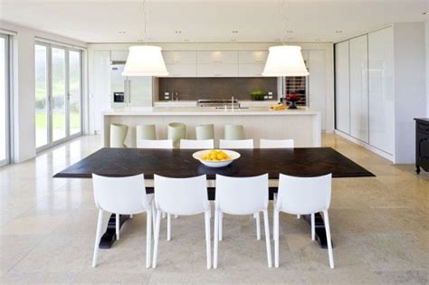 An open dining area illuminated by various styled pendants that hung over the smooth dark wood dining table surrounded by sleek white chairs on a beige area rug. Kitchen Dark wood table with white chairs | Dark wood ...