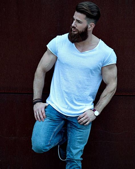 A Bearded Man Leaning Against A Wall With His Hands In His Pockets