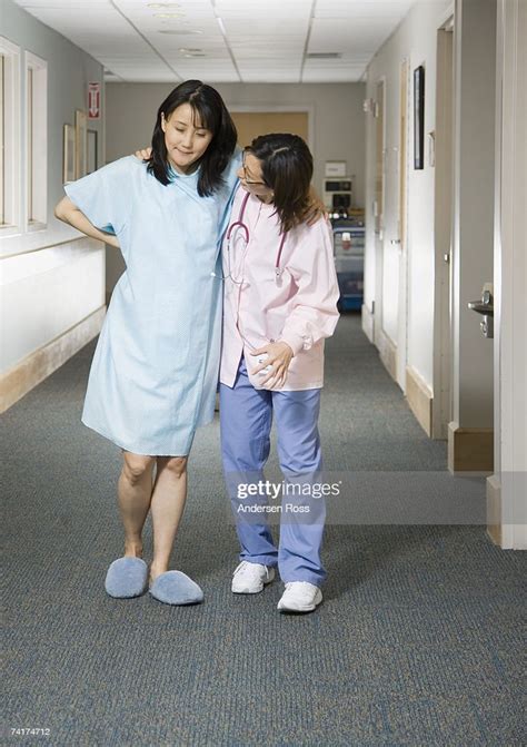 Female Nurse Helping Pregnant Woman To Walk In Hospital Corridor High