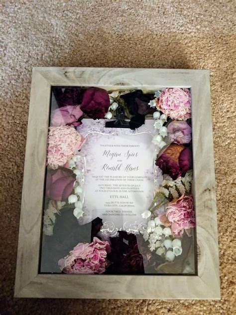 a wedding card in a frame with flowers on the floor next to it and an