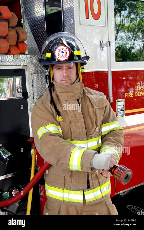 Male Firefighter Holding Fire Hose In Front Of Fire Truck Wearing