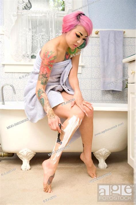 Woman In Towel Shaving Her Leg On Side Of The Bathtub Stock Photo