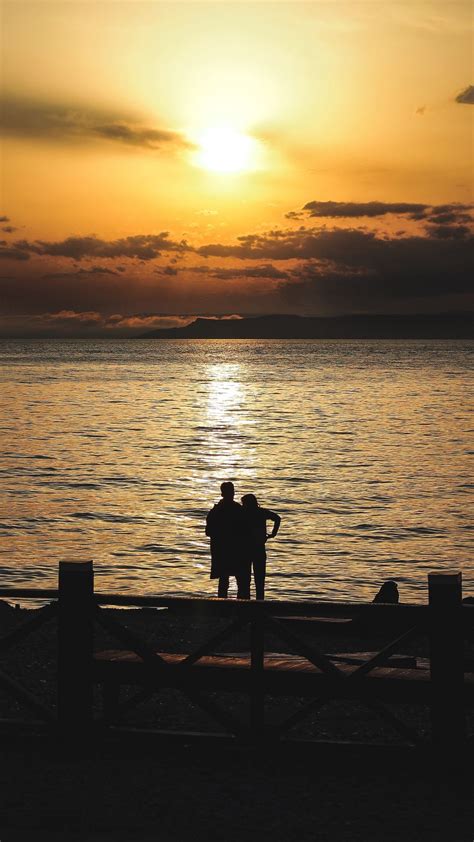 Download Wallpaper 938x1668 Silhouettes Sunset Couple Sea Horizon