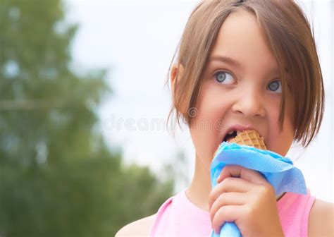 niña bonita que come lamiendo el helado grande en la risa feliz del cono de las galletas en