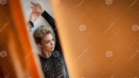 powabna młoda blondynki kobieta w czarnej bluzce pozuje provocatively przez pomarańczowych