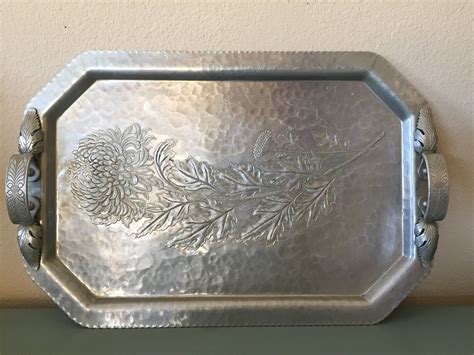 an ornate silver tray with pine cones and leaves engraved on the bottom sitting on a table
