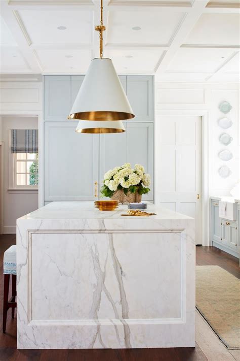 A White Kitchen With Marble Counter Tops And Gold Pendant Light Hanging