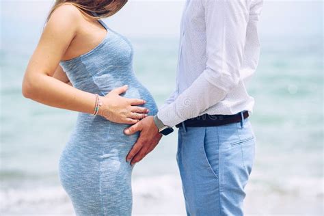 Loving Couple On The Beach Touching Pregnant Woman`s Belly With Love