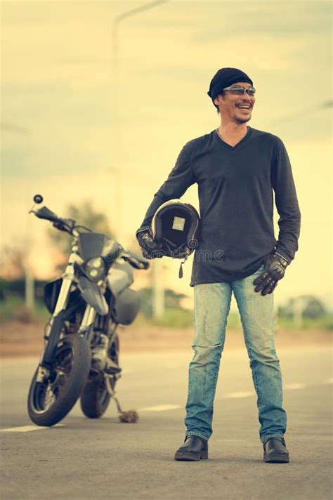 Portrait Of Man Biker Standing On Road With Motorcycle Stock Photo