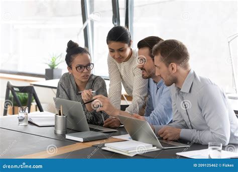 Mixed Raced Millennial Employees Talking At Shared Desk With Laptops