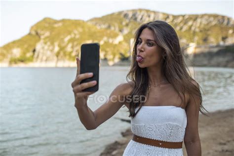 Young Woman Sticking Out Tongue While Taking Selfie Through Smart Phone At Pantano De Santa Ana