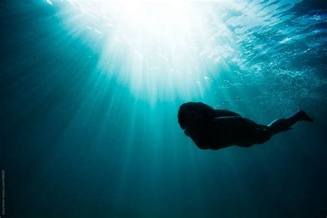 Girl Swimming Under Water In The Ocean As The Sun Rays Shine Down By