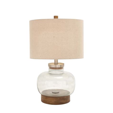 A Glass Lamp With A Wooden Base And A Beige Linen Shade On The Top Of It