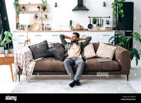 Satisfied Relaxed Young Indian Man Chilling On Sofa In Living Room