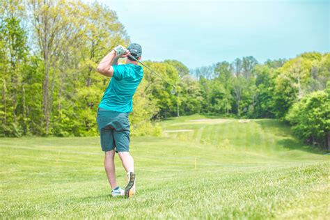 A Man Swinging A Golf Club On A Lush Green Field With Trees In The