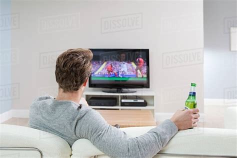 Young man watching football on television with beer bottle - Stock ...