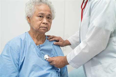 Doctor With Stethoscope Checking Senior Or Elderly Old Lady Woman Patient While Sitting On A Bed